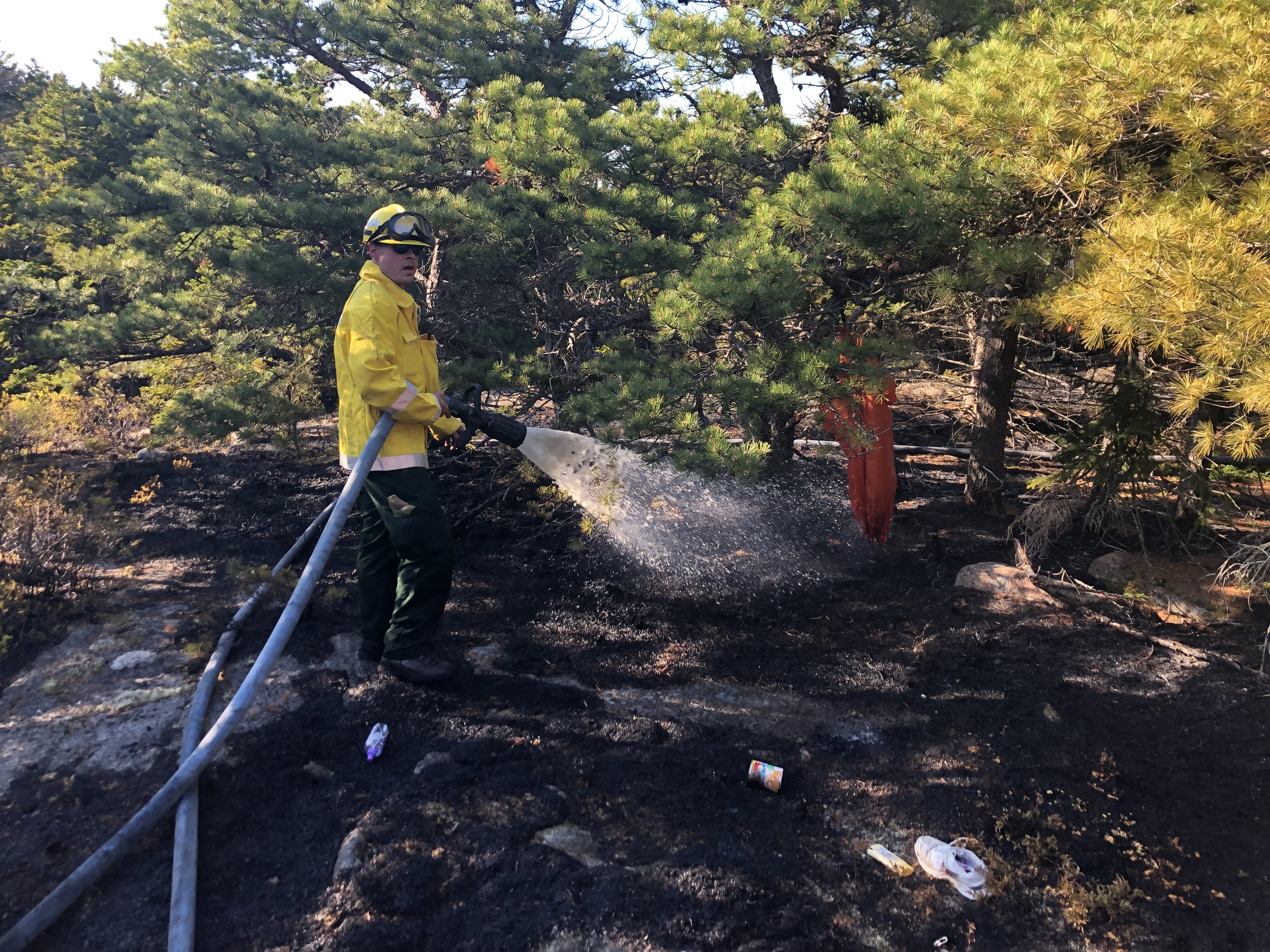 Firefighter hoses down burned area with water