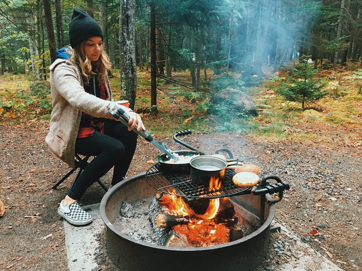 Woman makes breakfast on a campfire in a park campground Woman makes breakfast on a campfire in a park campground