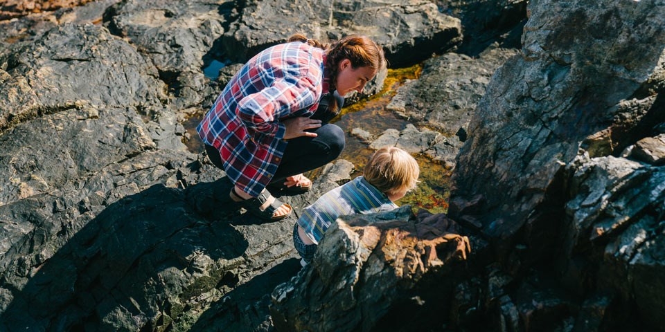 Woman and child crouch to explore among rocks Woman and child crouch to explore among rocks