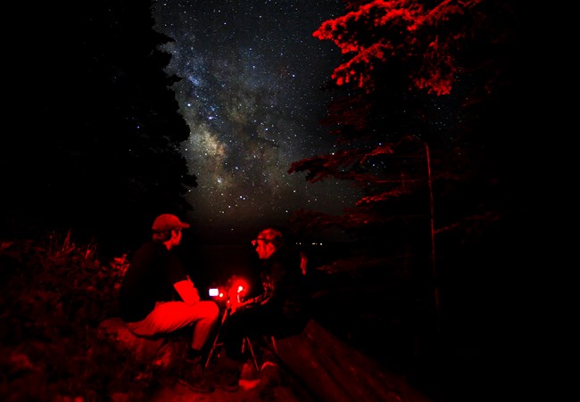 Two people use red lights while taking photos at night