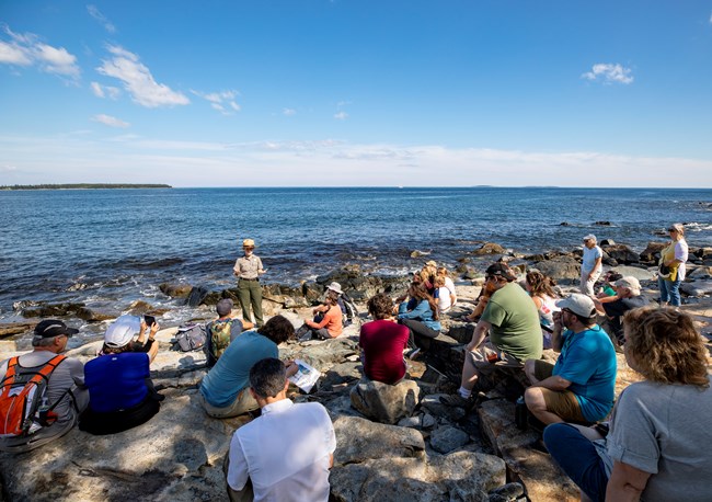 Visitors sit on a coastline for a ranger program