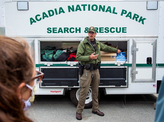 A ranger talks in front of a vehicle with open cargo containers. On it are the words Acadia National Park Search & Rescue