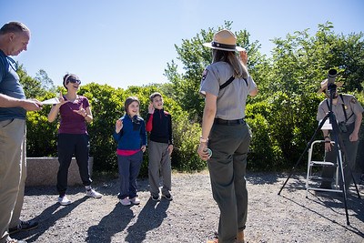 A park ranger holds up her hand while two kids hold up their hands in front of her.