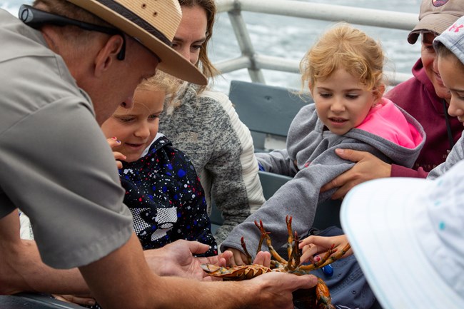 a ranger shows children the underside of a lobster on a boat