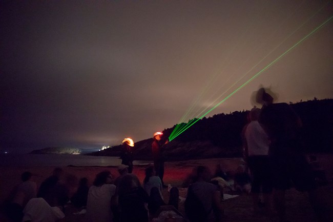 dark photo of rangers with glowing lasers pointing at the night sky