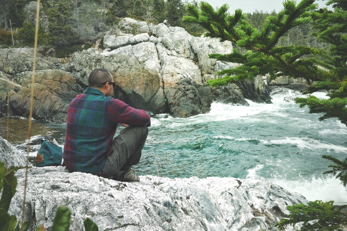 Man sits on rocky coastline facing an turbulent ocean inlet