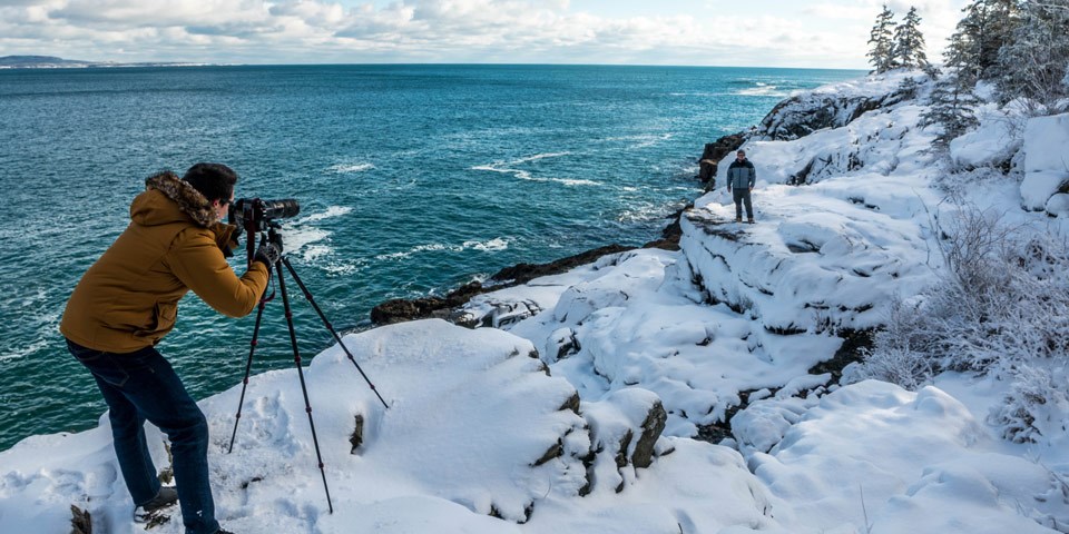 Photographer snaps portrait of man standing in snow along park coastline