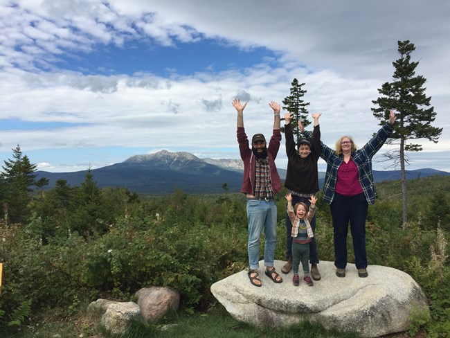 Four people stand with arms outstretched in foreground with mountain in background