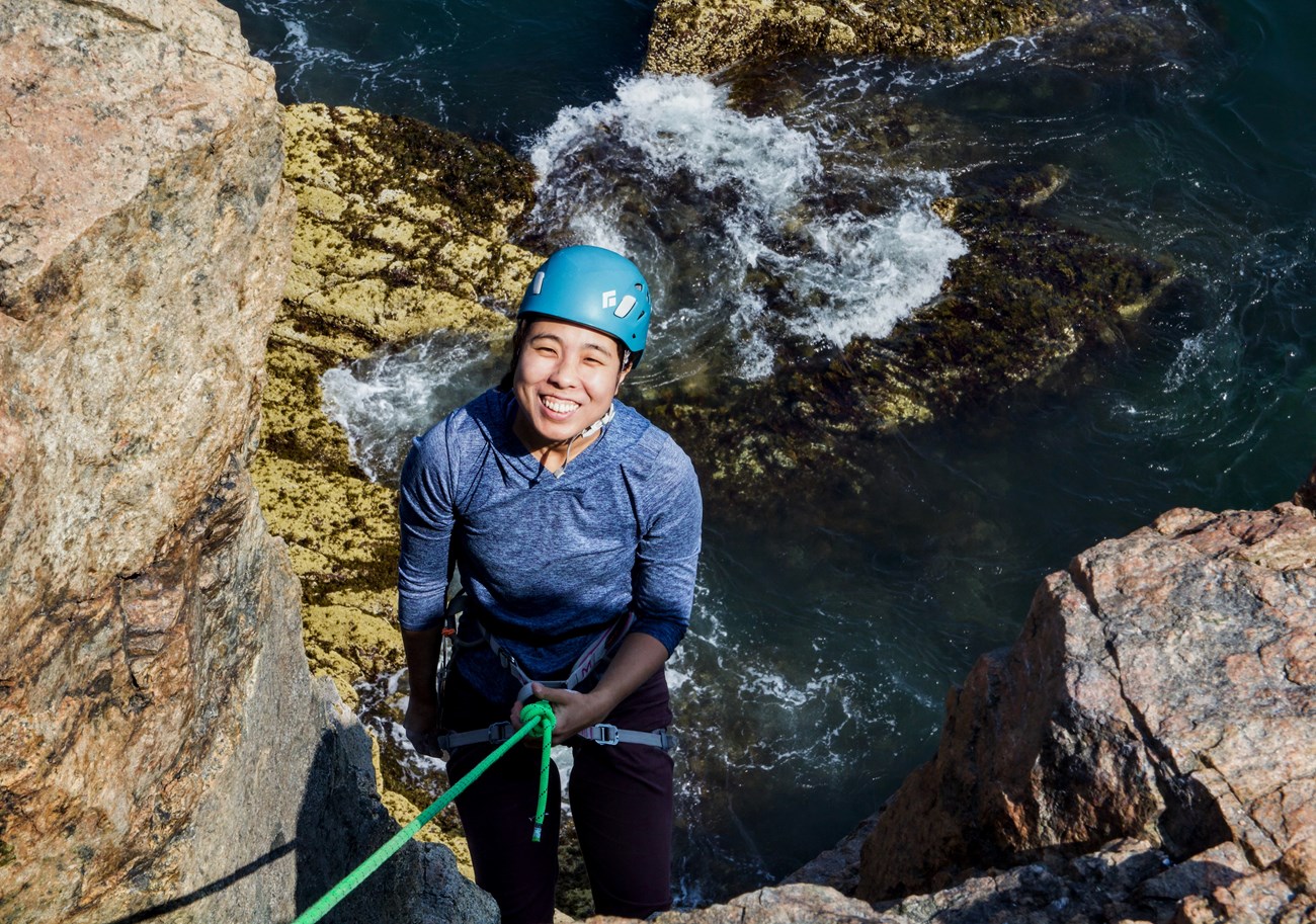A woman on a rope rappelling down ocean cliffs.