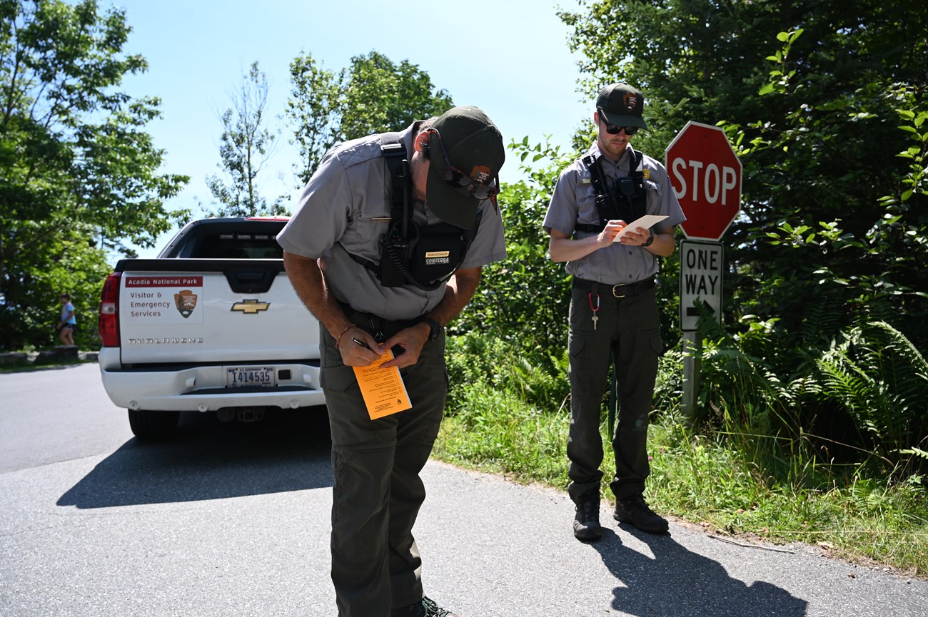 Two rangers writing tickets in front of an emergency services truck.