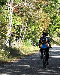 Man bikes on carriages roads against backdrop of fall leaves.