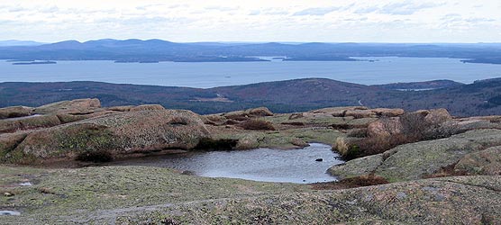Rocky mountain top with standing water and view of ocean and islands in background