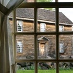 One New England saltbox-style house with brown siding viewed through a historic multi-pane window