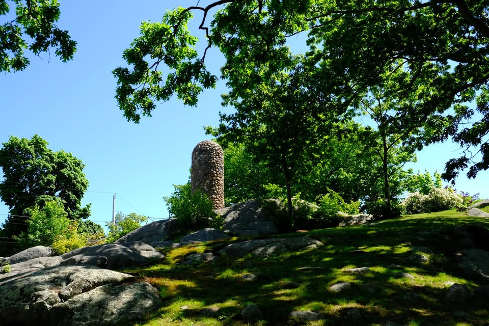 The Abigail Adams Cairn on Penn's hill marks the place Adams and her children watched the Battle of Bunker Hill unfold. A stone monument stands on top of a rocky hill, framed by leafy trees