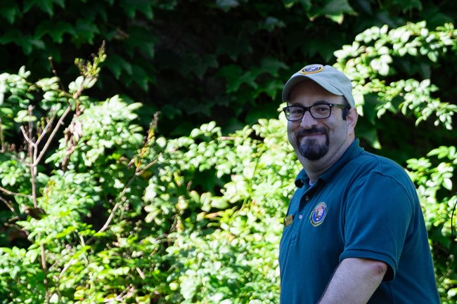 A man wearing a volunteer shirt and hat smiles at the camera