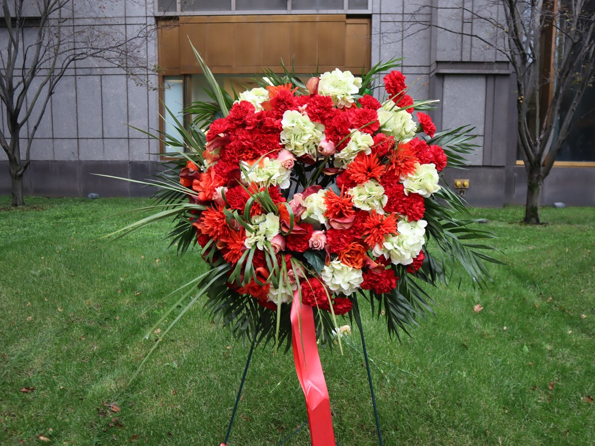 A wreath of red, pink and white flowers with greenery is placed on a burial mound.