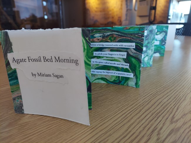 Lines of poetry are pasted on acordian-folded, multi-colored paper titled, "Agate Fossil Bed Morning by Miriam Sagan."