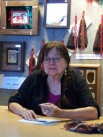 A woman with short brown hair and glasses sits at a table with a paper on the desk.