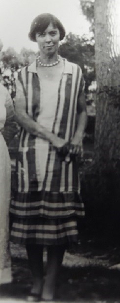 Young woman with short, bobbed hair cut under her ears wears a collared, striped dress & smiles at us.