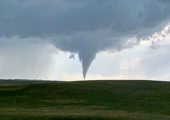 Dark gray tornado under gray clouds over green rolling hills