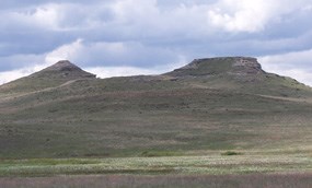 The green Fossil Hills in the distance display rock outcroppings under a blue cloudy sky.