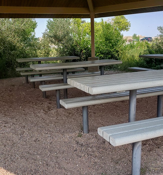 Picnic tables under a canopy structure. Gravel surface beneath.