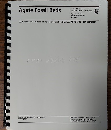 White spiral bound booklet. Across the top: Agate Fossil Beds; 2020 Braille transcription of visitor information brochure. Across the bottom: This edition is a Unified English Braille transcription. Center in Braille: Agate Fossil Beds.
