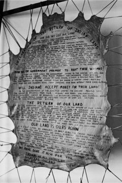 Text of a proclamation written on hide, stretched with string to a wooden frame. Some visible phrases include: "How does the government propose to right these wrongs?"; "Will Indians accept money for their land?"; "The return of our land"