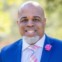 Bald man with goatee and blue suit smiles at camera.