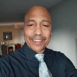 Bald Black man in button-down shirt and tie takes selfie.