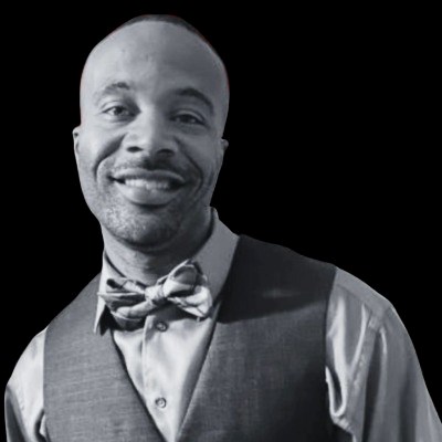 Bald African American man in bowtie and vest smiles at camera.