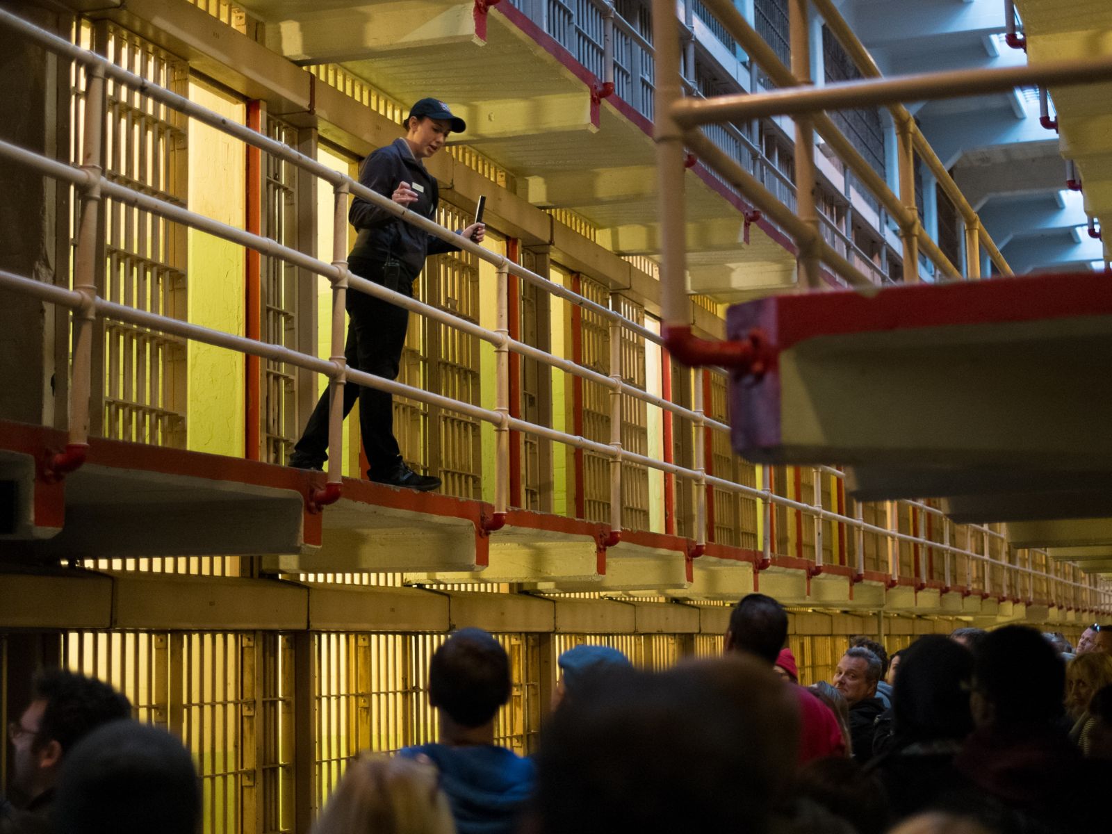 Park Ranger stands on second tier of a prison cell house, learning over railing to talk to crowd below.