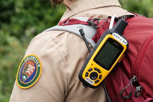 a radio clipped onto the backpack of a person wearing a shirt with a volunteer patch on their sleeve.