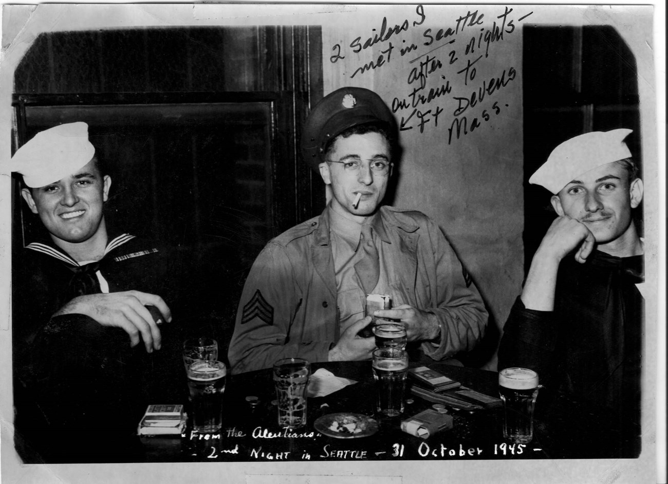 Al and sailors three men in uniform pose for the camera while playing cards. handwritten text reads "2 sailors I met in Seattle after 2 nights on train to Ft Devens Mass."