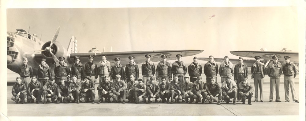 two rows of uniformed men pose with airplanes