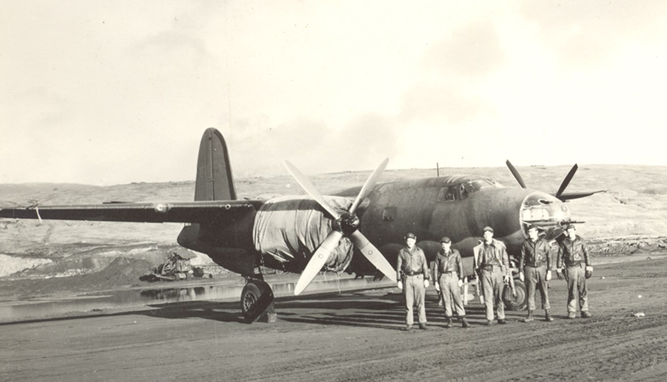 Plane on runway with group of men standing in front.