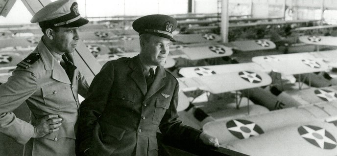 historic photo of two uniformed men looking over parked airplanes