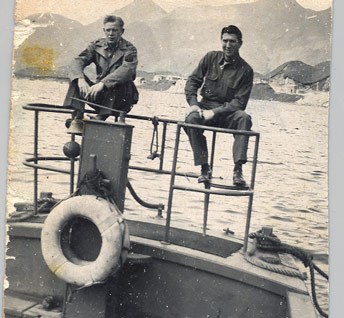 Historic image of two men sitting on the railing of a boat, mountains in the background