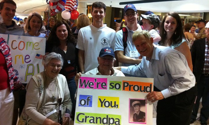 multi-generational family surrounding two elderly individuals with signs and balloons