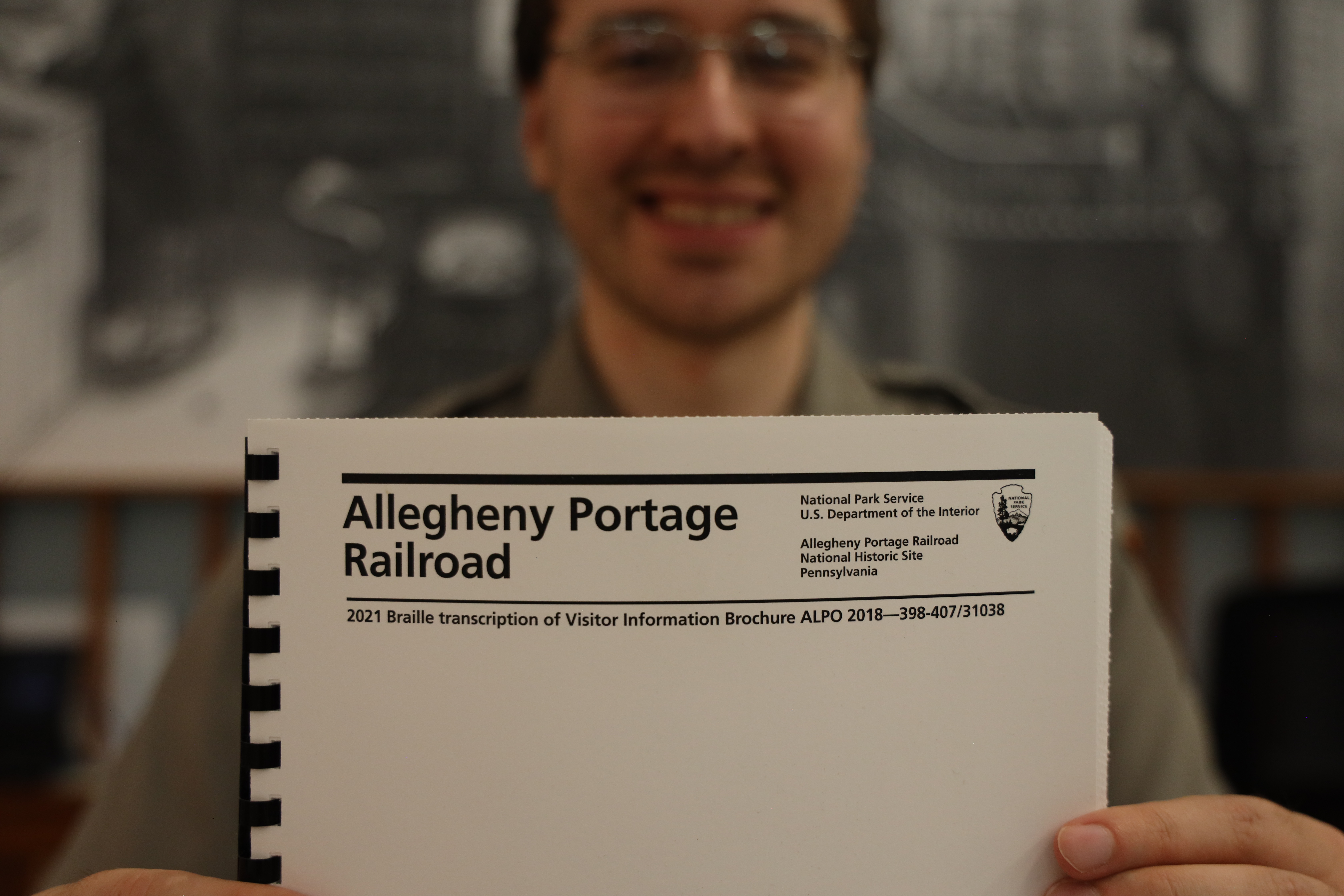 A park ranger holding up the Allegheny Portage Railroad Historic Site braille park brochure.
