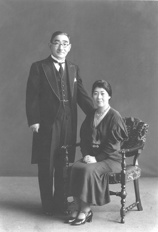 rev and mrs wada A woman sitting in a chair and a man standing next to her