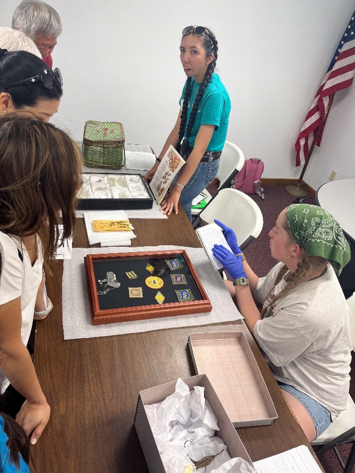 Two young women at a table full of artifacts, showing them to a group of people.