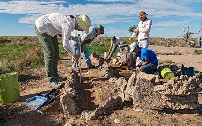 Individuals participating in excavations durigroung the 2022 University of Denver field school.  Individual in forend is measuring pond feature while several other record data.