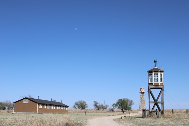 A barrack, water tower, and guard tower in a grassy field.