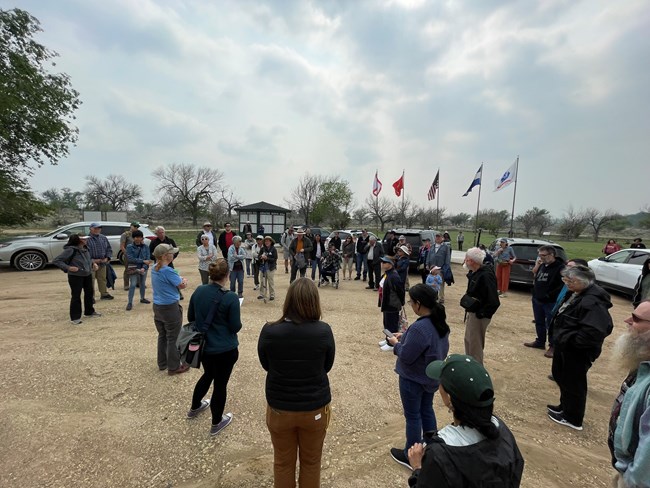 Group gathered near the park entrance visitor use area.  Five flags and Amache Honor roll can be seen in the background.