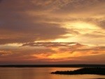 Oranges and browns swirl the cloudy sky at sunset with lake below.