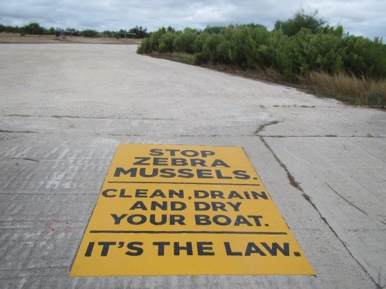 We all need to work together to protect Amistad Reservoir. Boat Ramp stencil about aquatic invasives stating "Stop Zebra Mussels. Clean, drain, and dry your boat. It's the law."