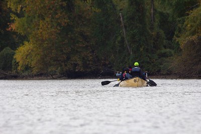 A canoe is in floating in a river with trees along the banks.