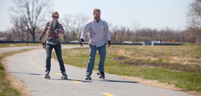 A man and woman smile as they roller skate on a paved trail by the Anacostia River. A man and woman smile as they roller skate on a paved trail by the Anacostia River.