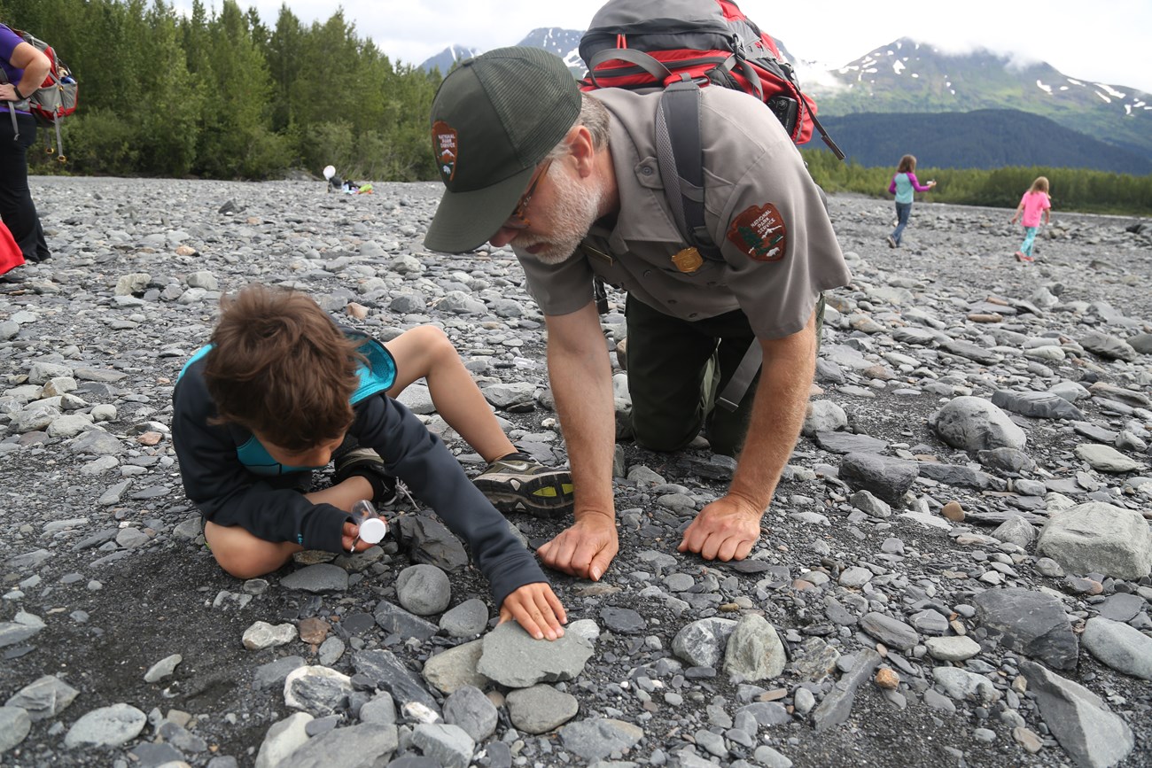 A ranger and a student investigate rocks in a river bed